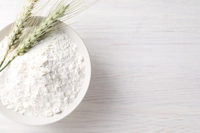 Photo of Green wheat spikes and flour on light wooden table, top view. Space for text
