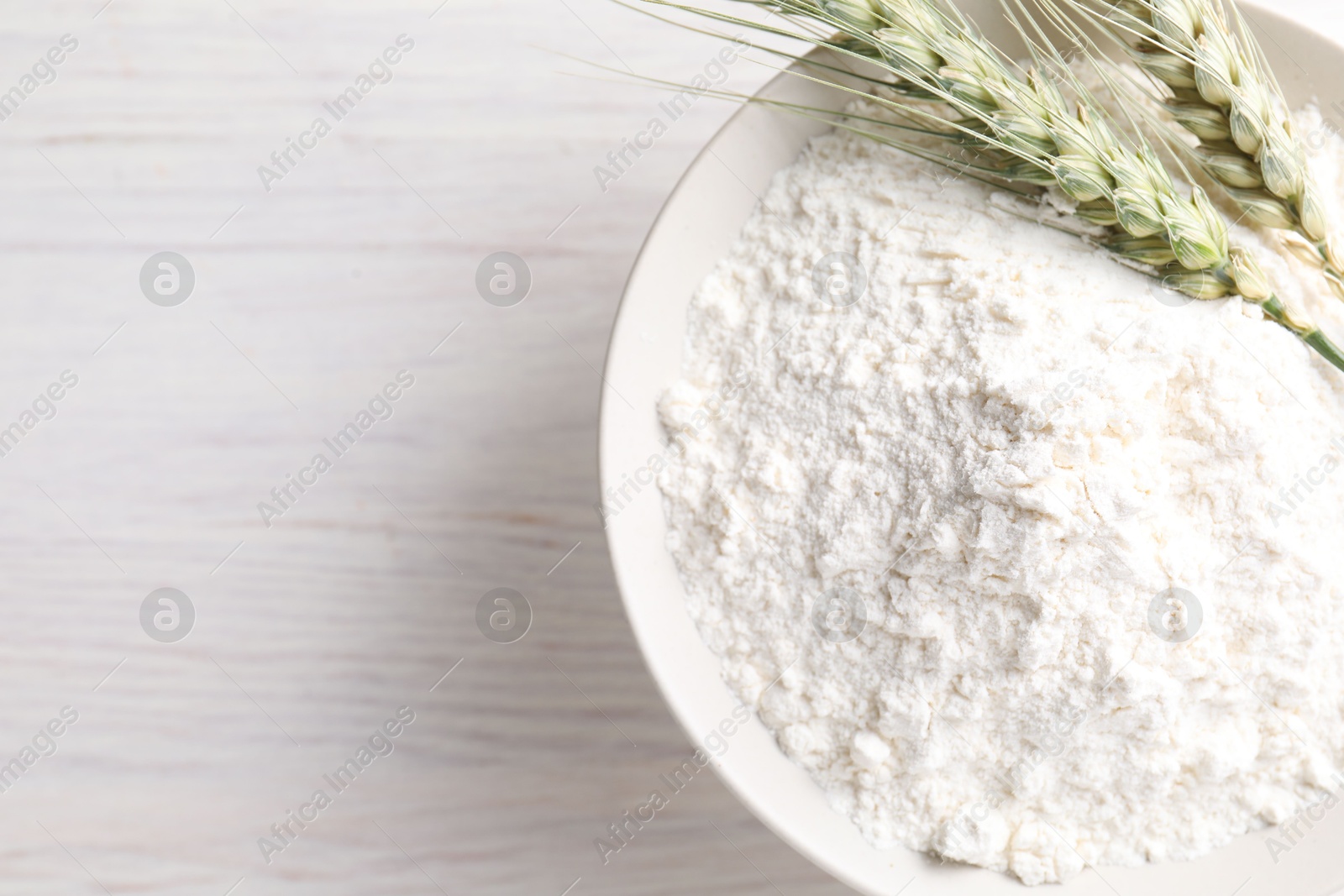 Green wheat spikes and flour on light wooden table, top view. Space for text Photo of Green wheat spikes and flour on light wooden table, top view. Space for text