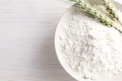 Photo of Green wheat spikes and flour on light wooden table, top view. Space for text