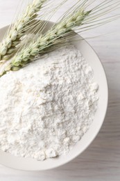 Photo of Green wheat spikes and flour on light wooden table, top view
