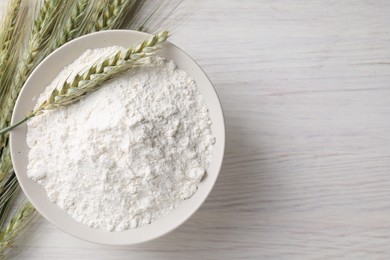 Photo of Green wheat spikes and flour on light wooden table, flat lay. Space for text