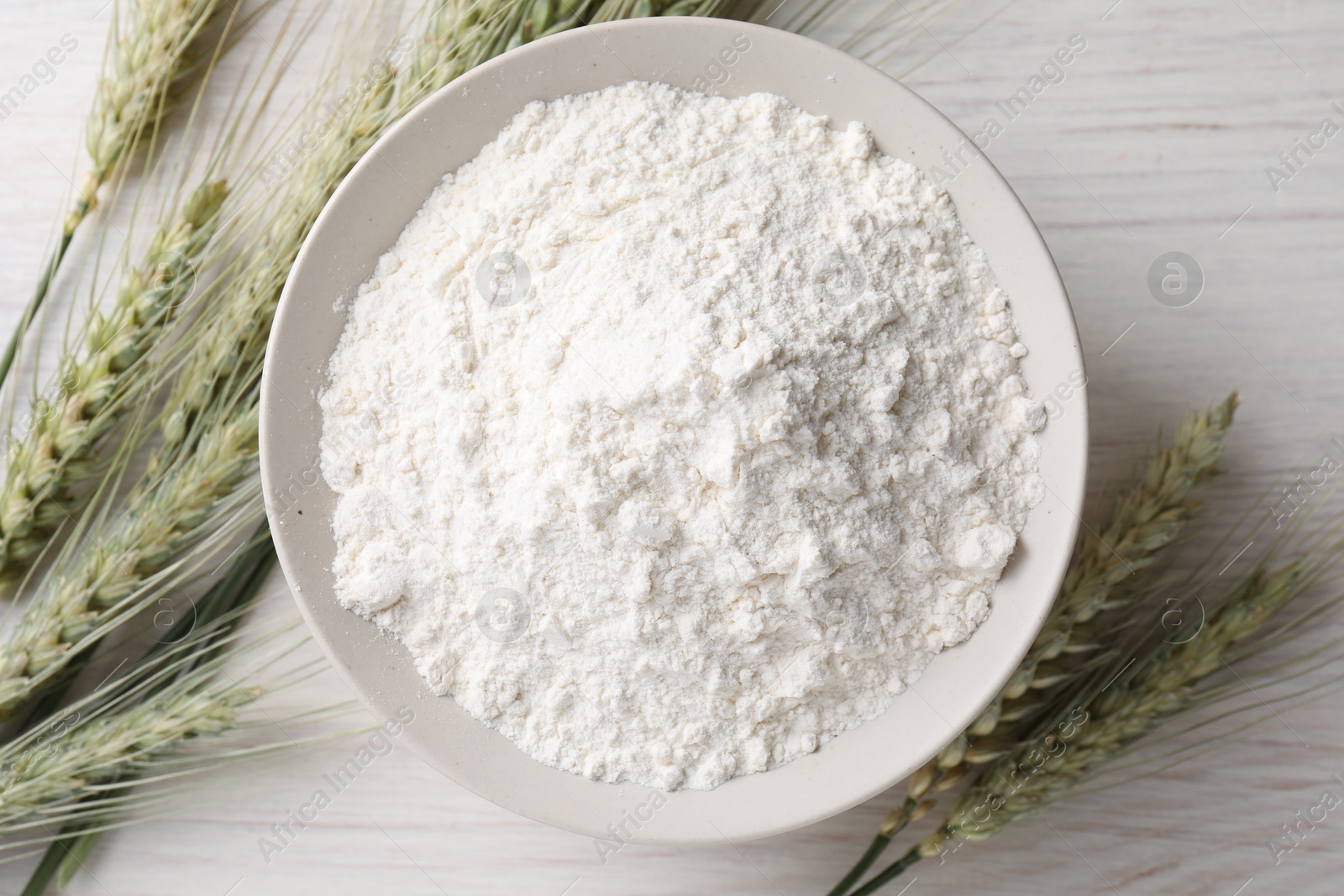 Green wheat spikes and flour on light wooden table, flat lay Photo of Green wheat spikes and flour on light wooden table, flat lay