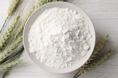 Photo of Green wheat spikes and flour on light wooden table, flat lay