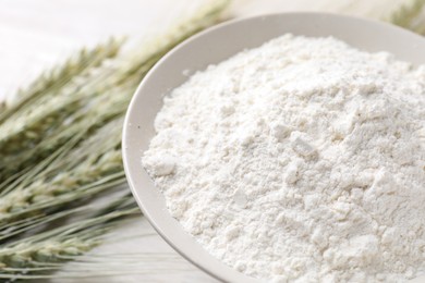 Photo of Green wheat spikes and flour on light table, closeup