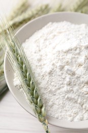 Photo of Green wheat spikes and flour on light table, closeup