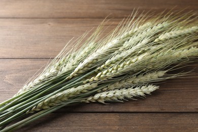 Photo of Many green wheat spikes on wooden table, closeup