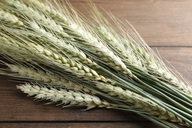 Photo of Many green wheat spikes on wooden table, closeup