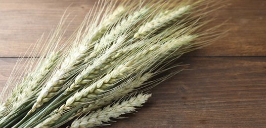 Photo of Many green wheat spikes on wooden table, closeup. Space for text