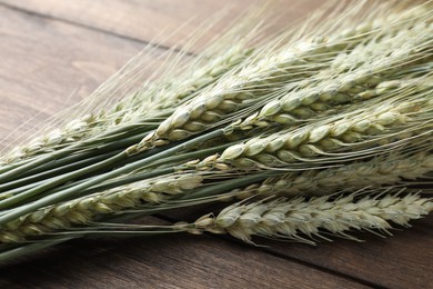 Photo of Many green wheat spikes on wooden table, closeup