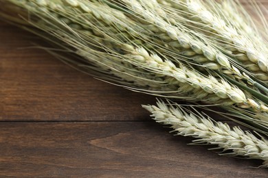 Photo of Many green wheat spikes on wooden table, closeup. Space for text