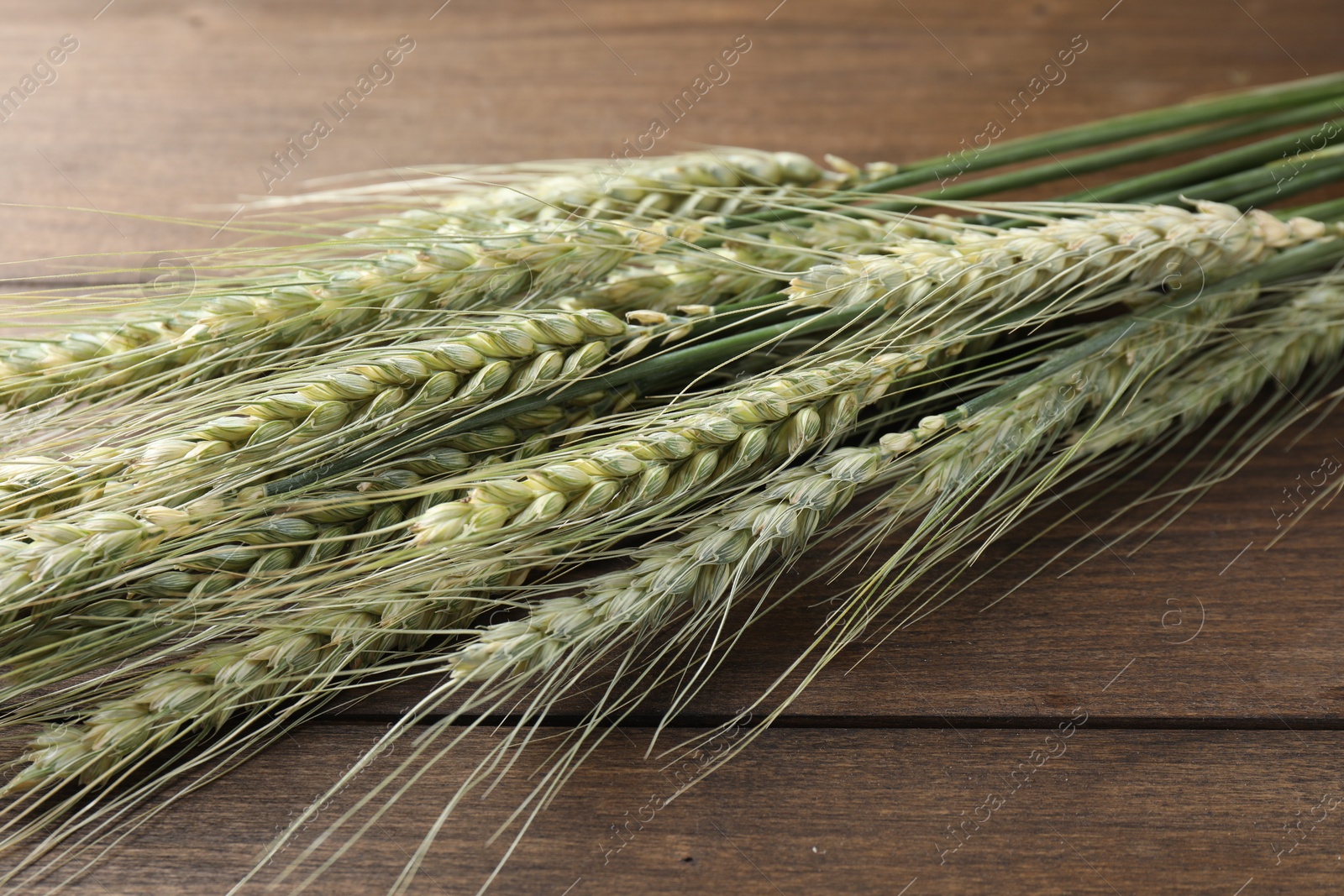 Photo of Many green wheat spikes on wooden table, closeup
