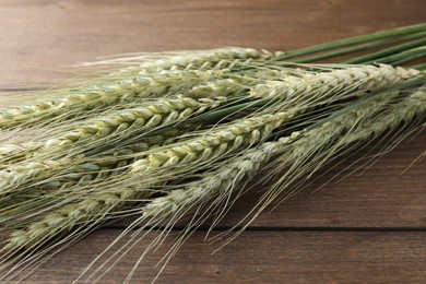 Photo of Many green wheat spikes on wooden table, closeup