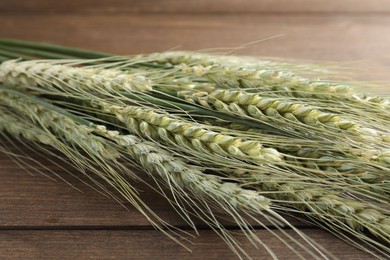 Photo of Many green wheat spikes on wooden table, closeup