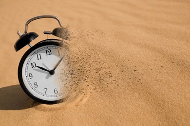 Image of Time running out. Black alarm clock dissolving in sand