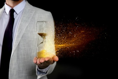 Image of Time running out. Hourglass dissolving in man's hand against black background, closeup