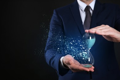 Image of Time running out. Hourglass dissolving in man's hands against black background, closeup