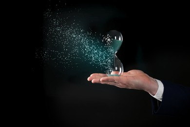Image of Time running out. Hourglass dissolving in man's hand against black background, closeup