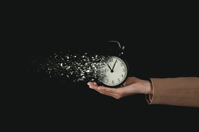 Image of Time running out. Alarm clock dissolving in woman's hand against black background, closeup