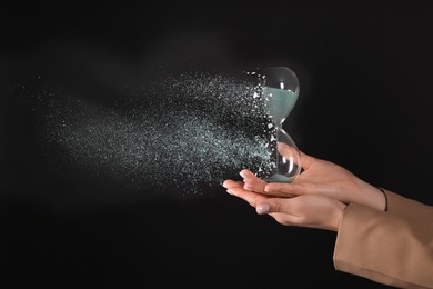 Image of Time running out. Hourglass dissolving in woman's hands against black background, closeup