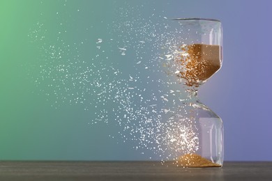 Image of Time running out. Hourglass dissolving on table against color background