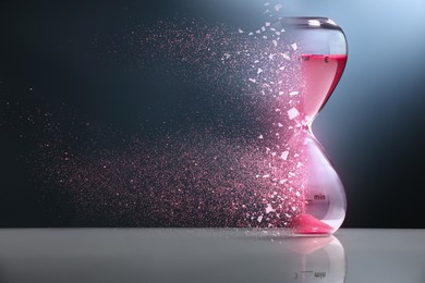 Image of Time running out. Hourglass dissolving on table against dark background