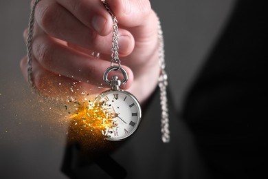 Image of Time running out. Pocket watch dissolving in man's hand against grey background, closeup