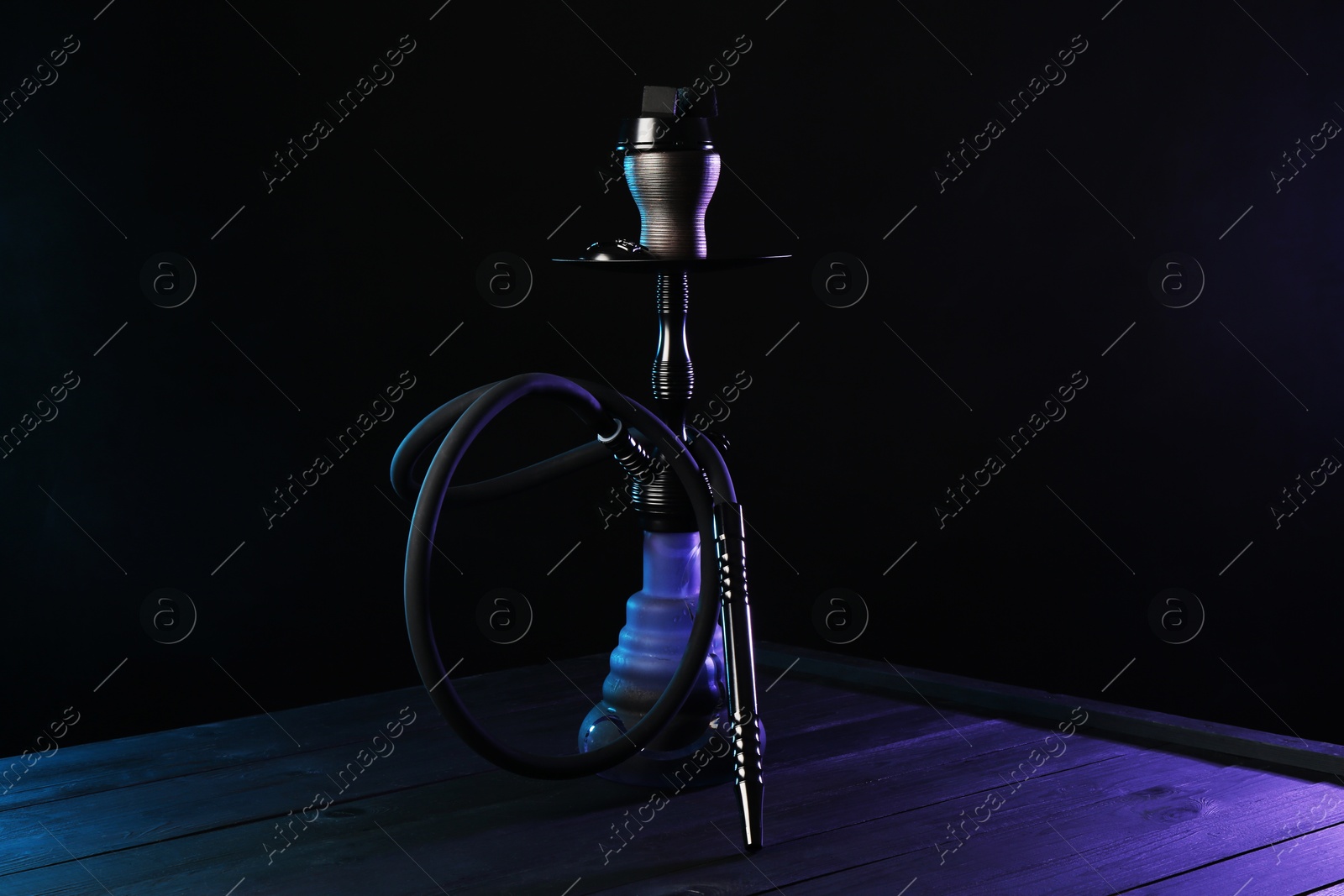 Hookah on wooden table with smoke in color lights against black background Photo of Hookah on wooden table with smoke in color lights against black background