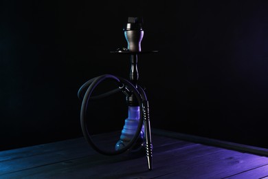 Photo of Hookah on wooden table with smoke in color lights against black background