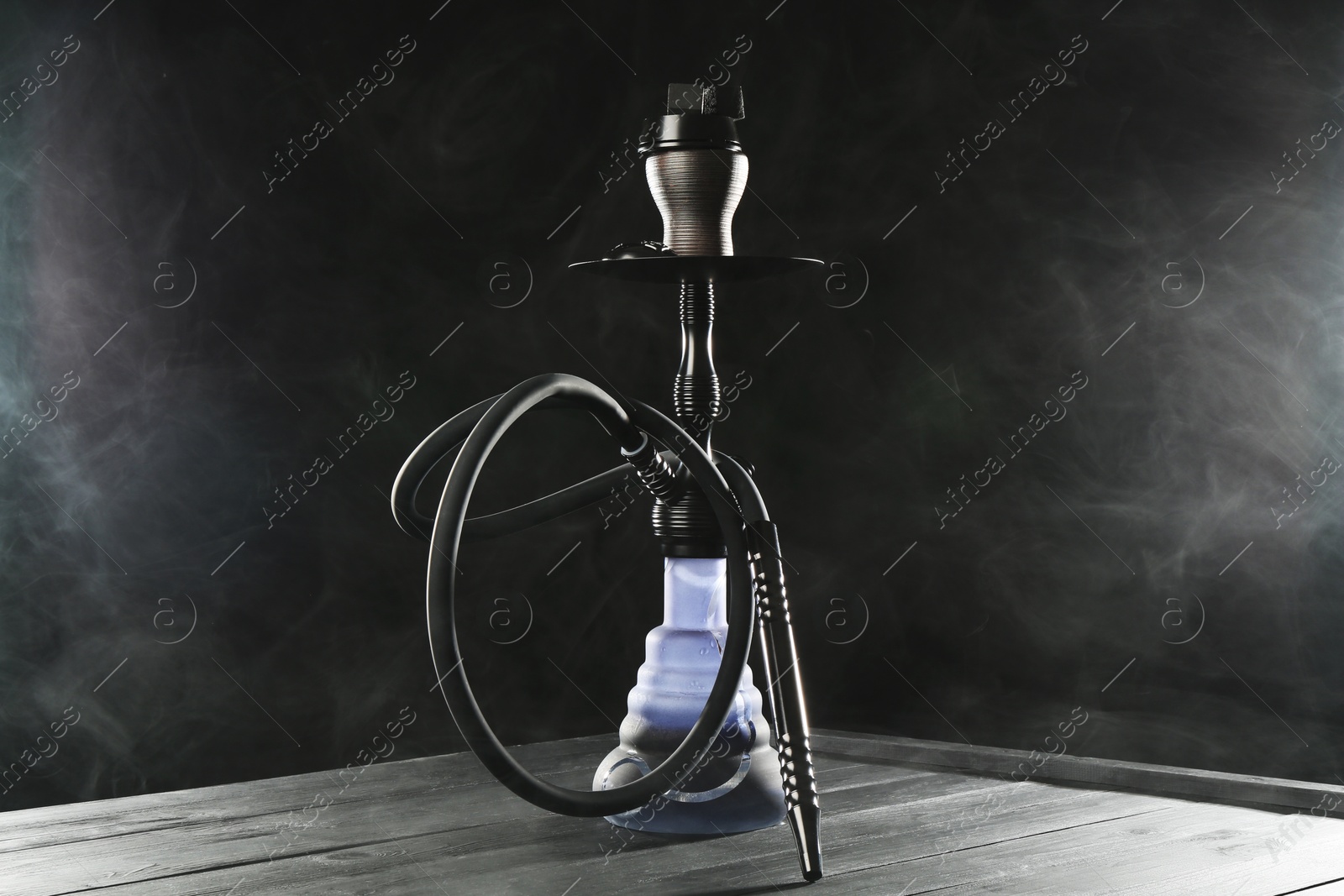 Hookah on wooden table with smoke against black background Photo of Hookah on wooden table with smoke against black background