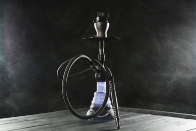 Photo of Hookah on wooden table with smoke against black background