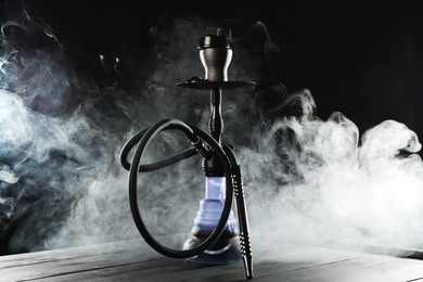 Photo of Hookah on wooden table with smoke against black background
