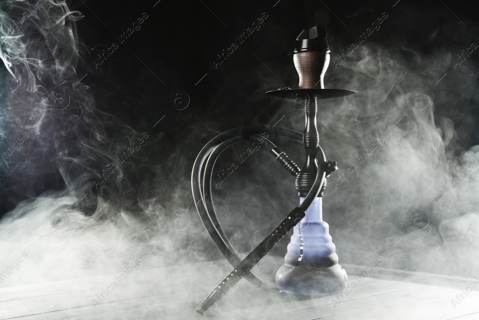 Hookah on wooden table with smoke against black background Photo of Hookah on wooden table with smoke against black background