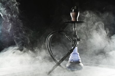 Photo of Hookah on wooden table with smoke against black background