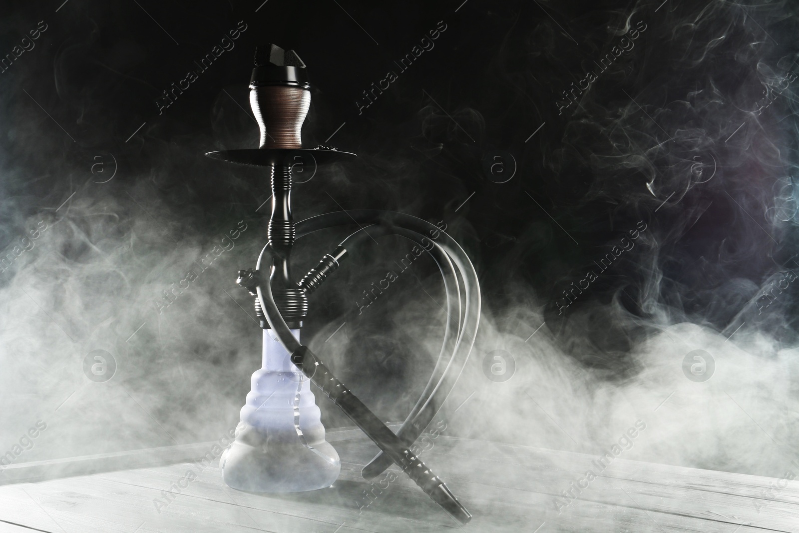 Hookah on wooden table with smoke against black background Photo of Hookah on wooden table with smoke against black background
