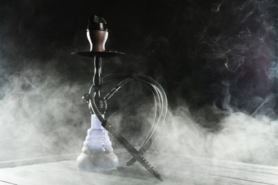 Photo of Hookah on wooden table with smoke against black background