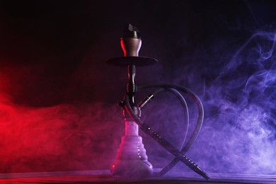 Photo of Hookah on wooden table with smoke in color lights against black background
