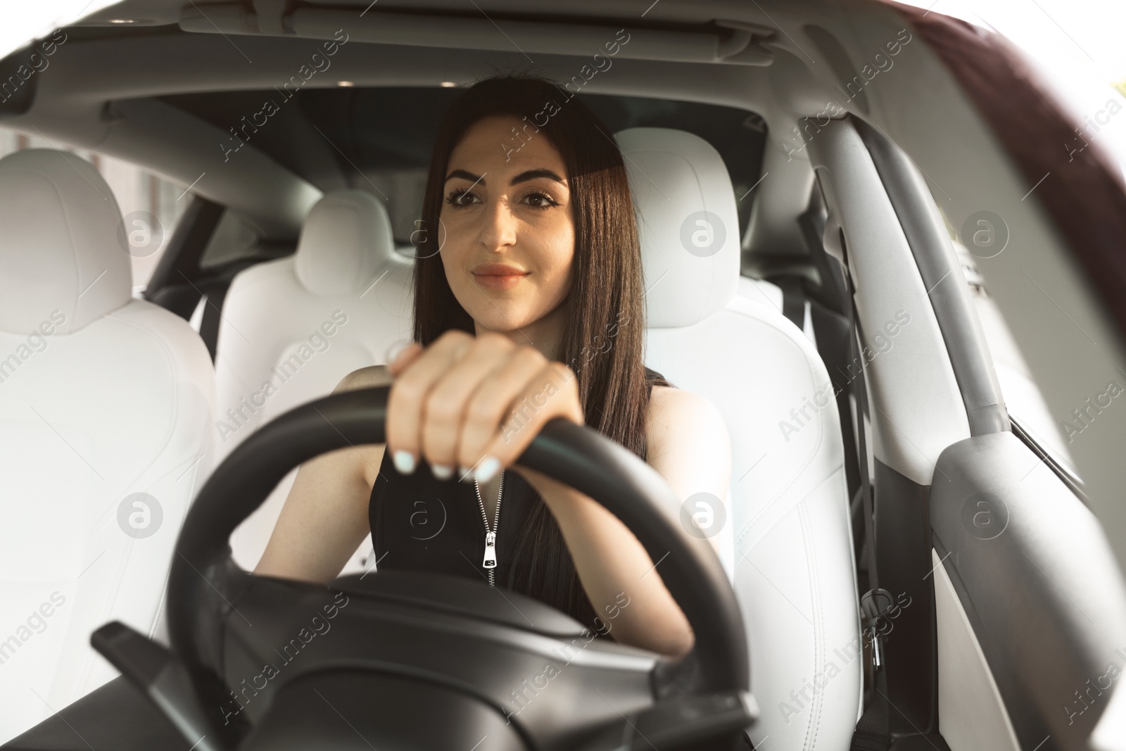 Photo of Woman behind steering wheel of modern car, view through windshield