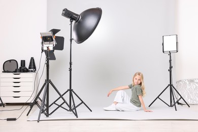 Photo of Little girl on light grey background in photo studio with professional equipment