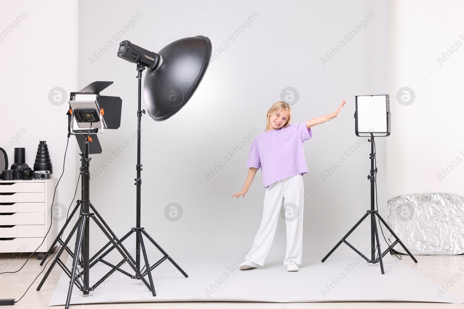 Photo of Little girl on light grey background in photo studio with professional equipment