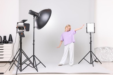 Photo of Little girl on light grey background in photo studio with professional equipment