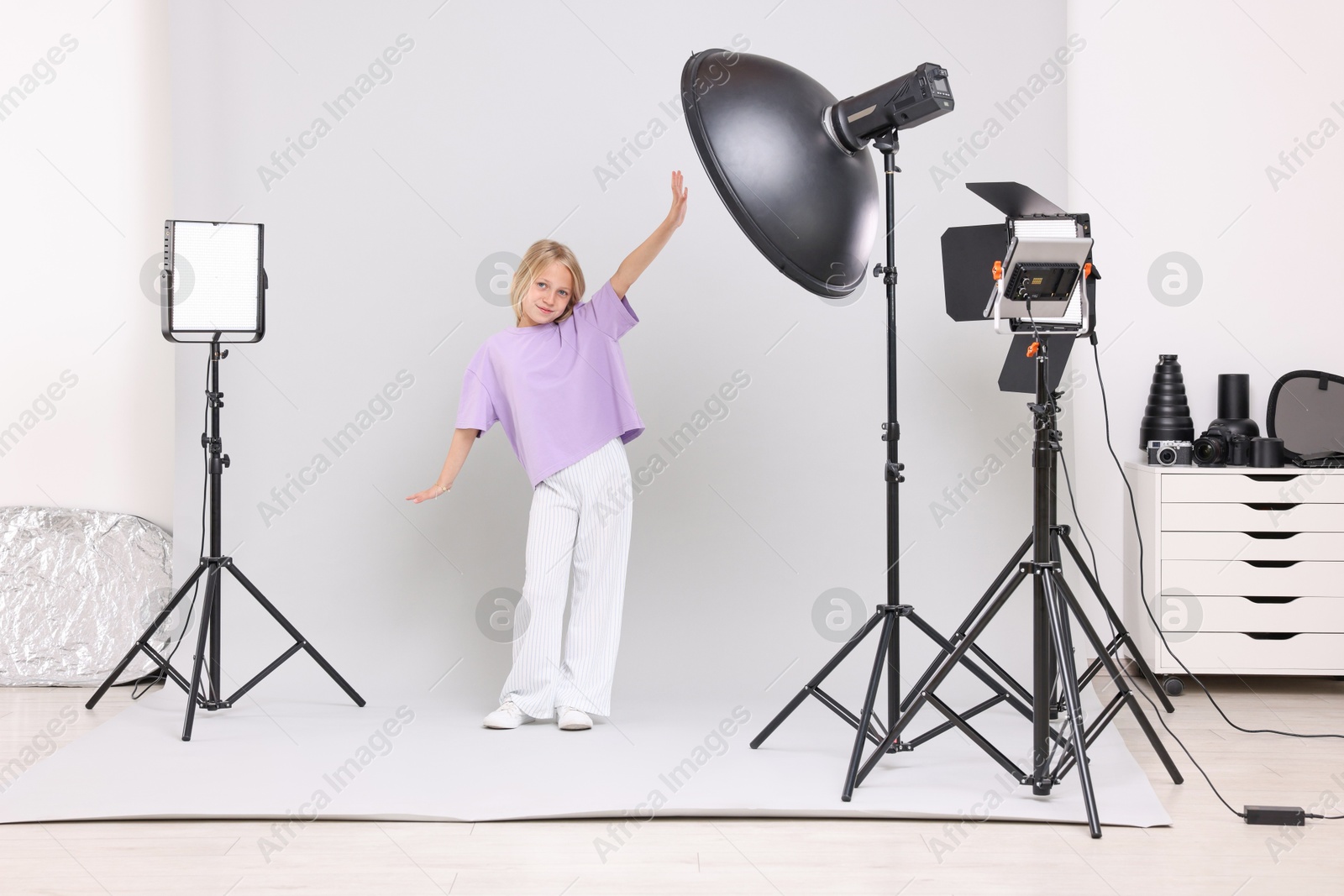 Photo of Little girl on light grey background in photo studio with professional equipment