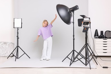 Photo of Little girl on light grey background in photo studio with professional equipment
