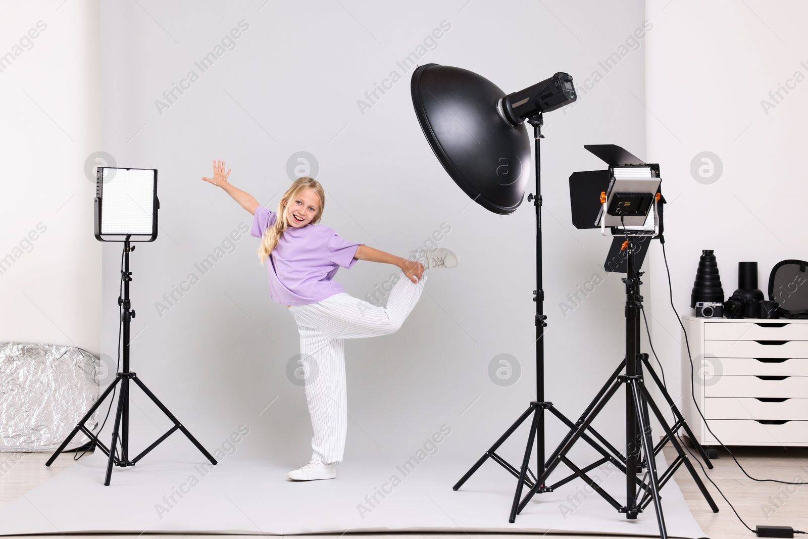 Photo of Little girl on light grey background in photo studio with professional equipment