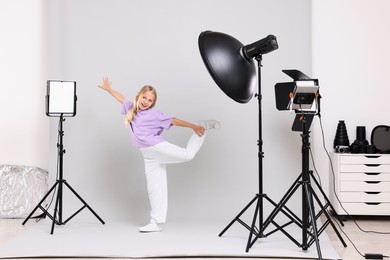 Photo of Little girl on light grey background in photo studio with professional equipment