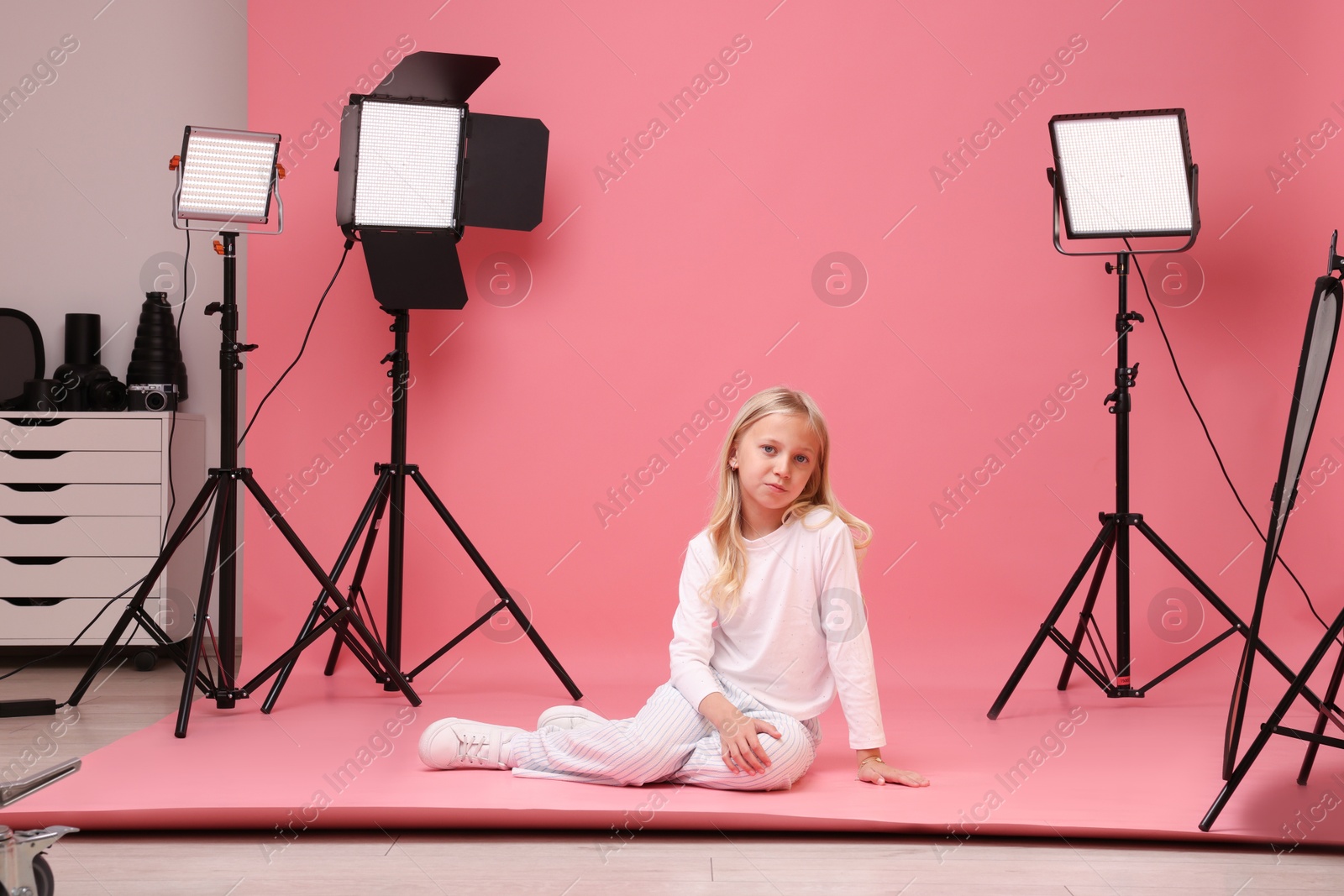 Photo of Little girl on pink background in photo studio with professional equipment