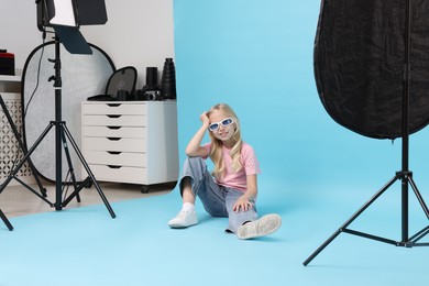 Photo of Little girl on light blue background in photo studio with professional equipment