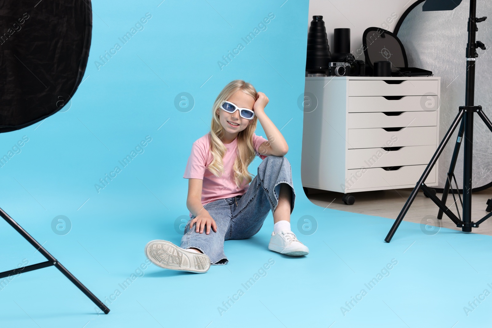 Photo of Little girl on light blue background in photo studio with professional equipment