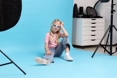 Photo of Little girl on light blue background in photo studio with professional equipment