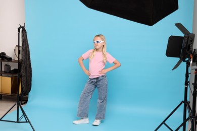Photo of Little girl on light blue background in photo studio with professional equipment