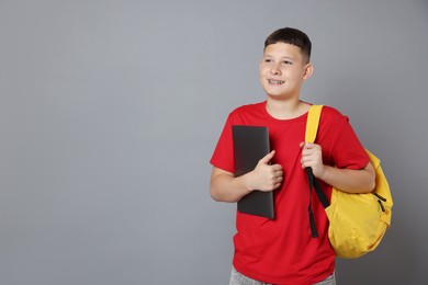 Photo of Teenage boy with laptop and backpack on grey background, space for text